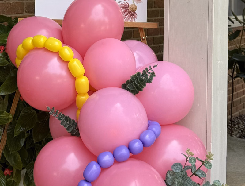 Close up of pink balloons with yellow and purple link balloons and eucalyptus