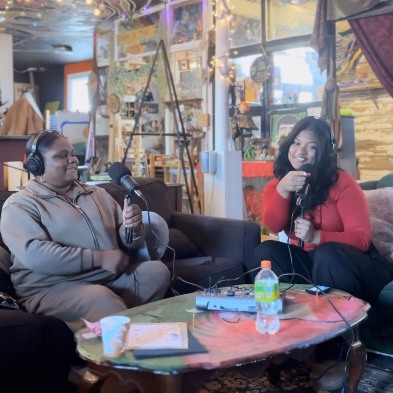 Two hosts recording in a colorful art studio with string lights