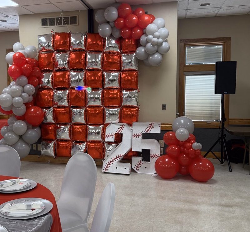 Red and silver foil balloon wall with red and gray garlands and large baseball marquee numbers